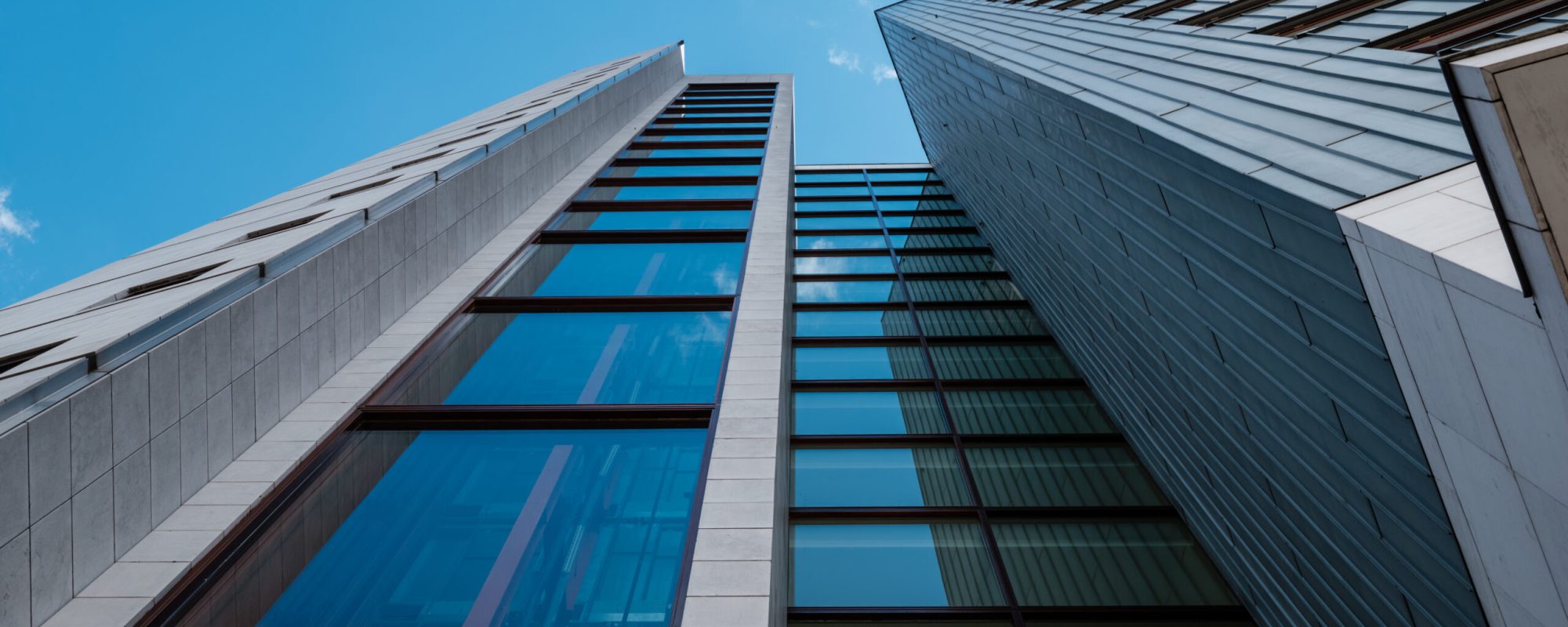 A low angle shot of a modern skyscraper with glass windows and with blue sky on the background